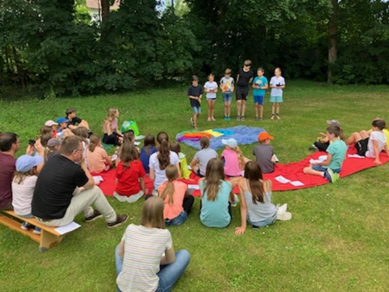 Kinder sititzen und stehen auf einer Wiese bei einer Andacht