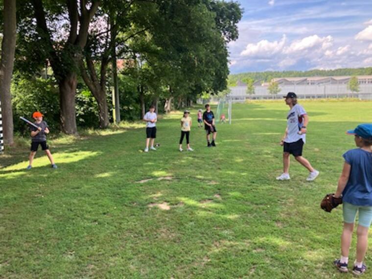 Kinder üben das Abschlagen eines Baseballs auf einer Wiese.